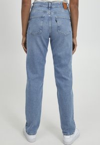 Jeans de mezclilla azules con cintura alta, corte recto, bolsillos traseros visibles y una etiqueta de cuero marrón en la cinturilla.