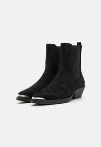Svarta mockaankelboots med låg staplad klack, elastiska sidpaneler och detaljer i metallic på tån. Slät yta och strömlinjeformat design.