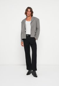 Gray blazer with notched lapels and two front pockets, paired with a white tank top and black straight-leg pants. Black ankle boots complete the look.