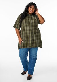 Camisa de cuadros verdes con cuello alto, mangas cortas; combinada con jeans de mezclilla azules y zapatos planos de tela negra.