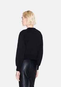 Felpa nera cropped con maniche raglan, polsini e orlo a costine. Tessuto in cotone misto morbido. Il modello indossa una gonna in pelle nera.