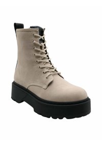 Stivaletto beige con finitura texturizzata, suola piatta nera, punta arrotondata e allacciatura nera; include un'ansia sul tallone.