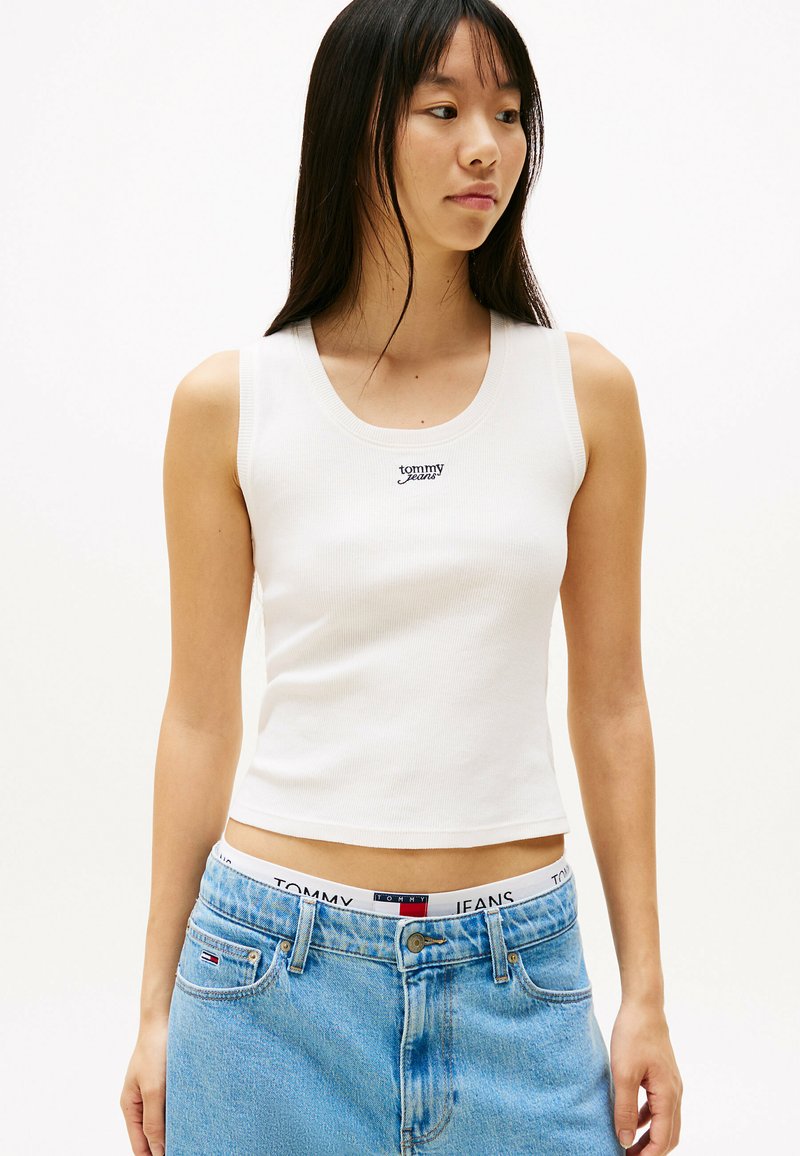 Witte, geribbelde tanktop met een ronde halslijn en het gecentreerde "Tommy Jeans" logo. In combinatie met lichtblauwe, high-waisted denim jeans.