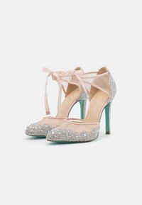 Tacchi alti beige con punta affusolata, decorati con strass trasparenti e un nastro rosa chiaro. Sides trasparenti e un accent heel color teal.
