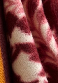 Soft wool fabric with a chevron pattern in shades of burgundy, pink, white, and a hint of mustard, shown close-up with folds and texture.