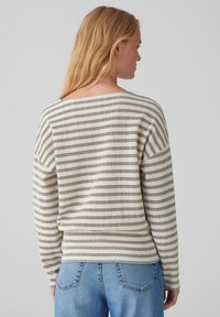 Lightweight, cream sweater with black vertical stripes, boat neckline, and long sleeves. Soft texture and relaxed fit. Worn with blue jeans.