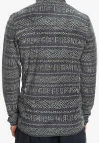 Polarowy półgolf w ciemnoszarym kolorze z jasnoszarymi geometrycznymi wzorami, długimi rękawami i zaokrąglonym dołem. Miękka faktura, brak widocznych zapięć lub detali.