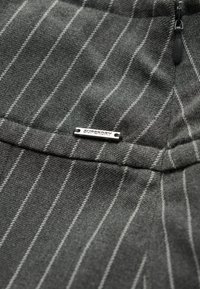 Grijs gestreepte stof met een gladde textuur, voorzien van een klein zilverkleurig "SUPERDRY" logo-label dat is vastgenaaid. Geaccentueerd met dunne witte strepen.