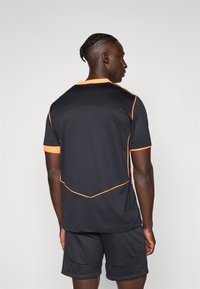 Svart atletisk trøye med korte ermer, med oransje detaljer på kragen og sømmene, kombinert med svarte shorts. Jevn tekstur.