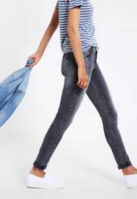 Jeans ajustados grises con cintura alta y puños enrollados, combinados con una camisa a rayas azul y blanca y zapatillas blancas sin cordones.