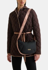 Giubbotto trapuntato marrone con rifiniture rosa chiaro, abbinato a una borsa nera a tracolla con logo dorato e tracolla decorata.