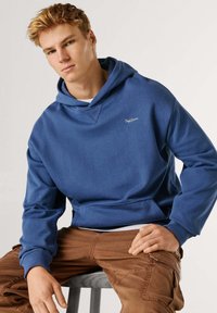 Niebieska bluza z kapturem o fakturowanym wykończeniu, z kapturem na sznurek i haftowanym logo na piersi, zestawiona z brązowymi spodniami cargo.