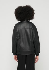 Jachetă bomber din piele neagră, croială supradimensionată, cu manșete și tiv striate. Textură netedă și detalii minime de cusături.