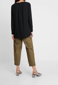 Top nero a maniche lunghe con scollo rotondo, abbinato a pantaloni larghi verde oliva e sandali con tacco a motivi bianco e nero.