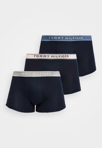Τρία σκούρα μπλε boxers με αντιθετικές μέσες σε γκρι, ανοιχτό ροζ και μπλε, καθένα με τη σήμανση "Tommy Hilfiger".