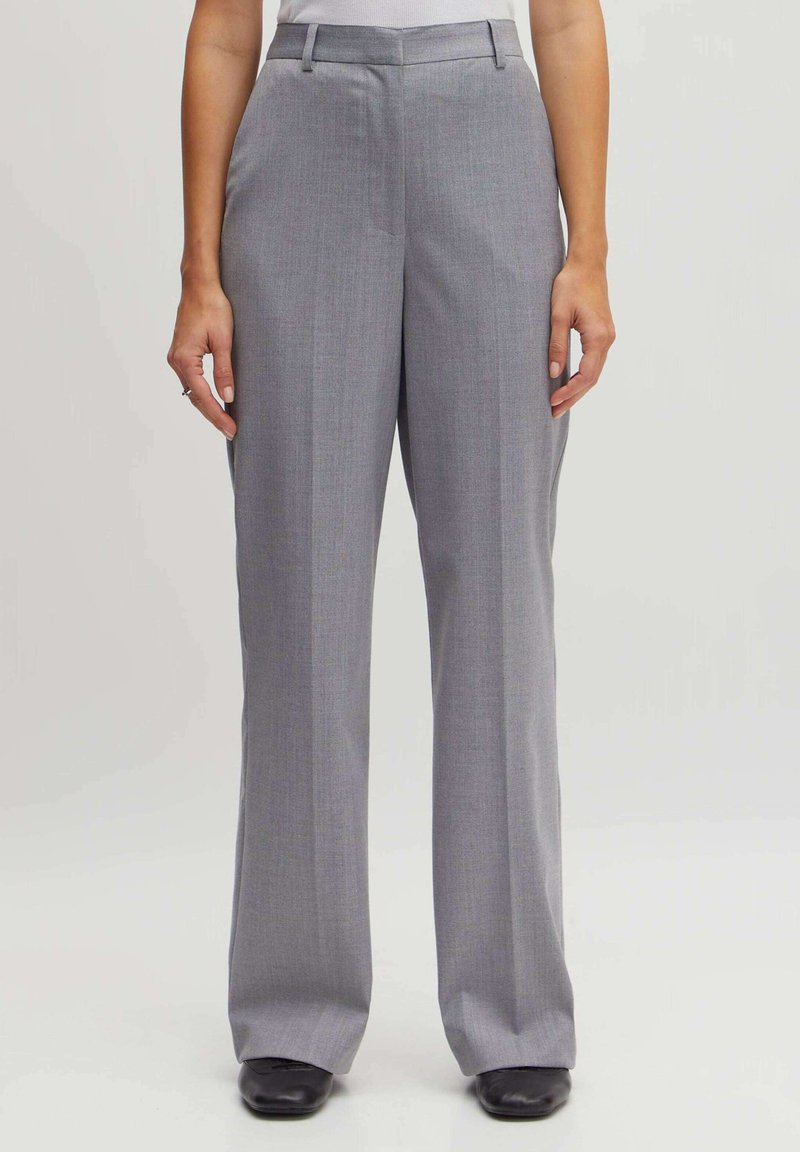Graue maßgeschneiderte Hose mit geradem Bein, die eine Bügelfalte auf der Vorderseite, Gürtelschlaufen und eine glatte Textur aufweist.