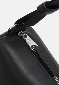 Czarna torba ze sztucznej skóry z srebrnym zamkiem błyskawicznym i metalowymi elementami, o gładkiej fakturze i materiałowym pasku do noszenia.