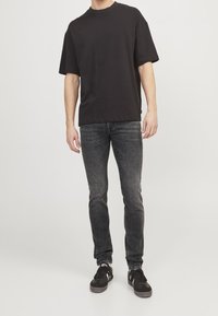 Camiseta negra de manga corta en tela de algodón, combinada con jeans ajustados de color gris oscuro. Los zapatos son negros con detalles blancos. Diseño minimalista.