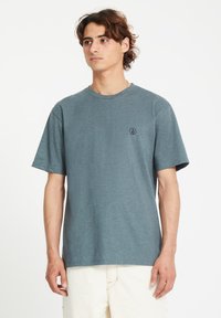 T-shirt à manches courtes, col rond, en tissu bleu clair, arborant un petit logo noir sur la partie gauche de la poitrine et une coupe décontractée.