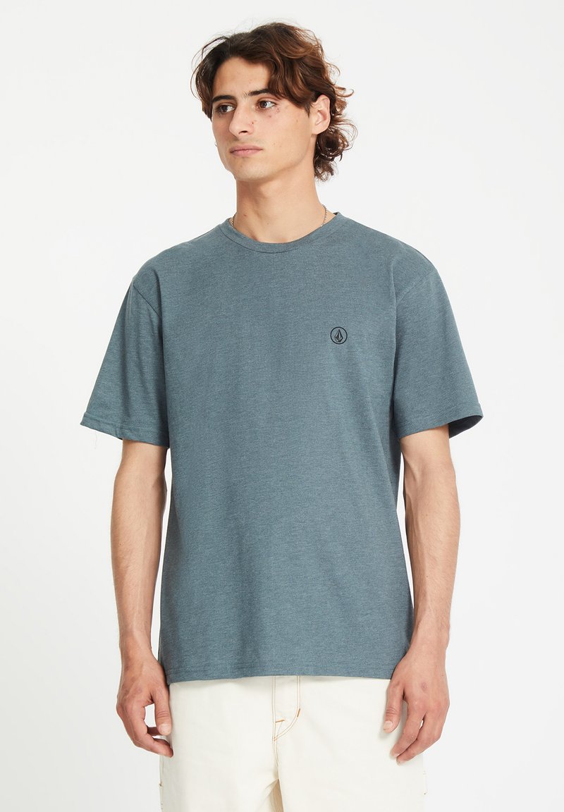 T-shirt à manches courtes, col rond, en tissu bleu clair, arborant un petit logo noir sur la partie gauche de la poitrine et une coupe décontractée.