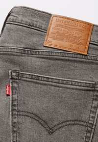Gray denim jeans with a brown leather patch displaying branding, red tab accent, and signature back pocket stitching detail.