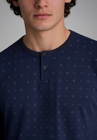 Polo shirt a maniche corte blu navy con scollatura rotonda, dotato di una chiusura a bottoni e un motivo geometrico ripetuto in blu chiaro e rosso.