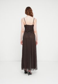 Maxi sukienka z przezroczystej brązowej tkaniny w białe kropki, regulowane cienkie ramiączka, dopasowana góra, zwiewna spódnica i boczne rozcięcie.