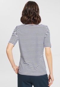 Camisa de manga corta y cuello redondo a rayas con rayas horizontales en azul marino y blanco, con un diseño ajustado. Sin logotipos ni patrones visibles.