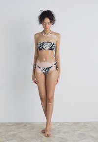 Bikini komplektas su be petnešėlių viršumi, juodai baltas abstraktaus rašto, atitinkamos kelnaitės su šoninėmis užrišamomis juostomis, pagamintas iš glotnaus audinio.