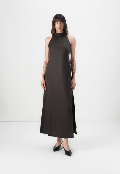 Vestido maxi sin mangas de color marrón oscuro con cuello alto y aberturas laterales, hecho de una tela suave. El modelo lleva zapatos negros tipo slip-on.