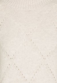 Knit sweater in light cream with a textured pattern of diamonds and small holes, featuring a ribbed neckline and soft, fuzzy material.