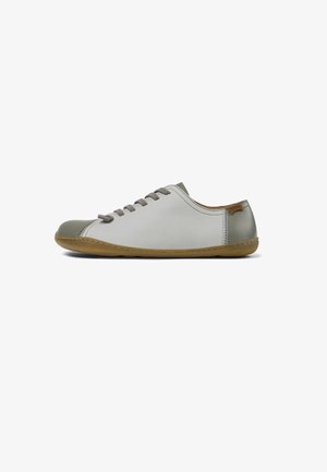 Zapatilla de cuero gris claro con puntera redondeada, cordones grises y un acento gris más oscuro en la puntera. Suela de goma en un color natural.