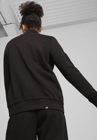 Sudadera negra de manga larga, con cuello redondo, puños y cintura acanalados. Presenta un pequeño logo de la marca en la parte inferior izquierda.