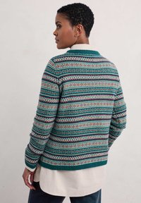 Groene gebreide trui met een patroon van meerkleurige strepen, geribbelde manchetten en een casual kraag. Gelaagd over een wit overhemd.