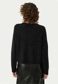 Svart stickad tröja med långa ärmar och rund halsringning, med en avslappnad passform och mjuk textur, i kombination med en svart läderskjorta.