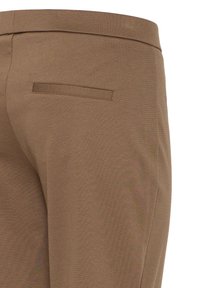 Gros plan sur un pantalon beige montrant la ceinture et une poche arrière passepoilée sur un tissu lisse.