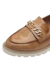Mocassin en cuir fauve avec une finition brillante et un accent de grosse chaîne en or sur la bride. Dispose d'une semelle en caoutchouc blanche épaisse.