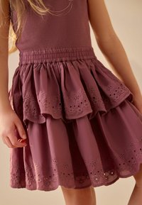 Ein lila Kleid mit einem gerippten Oberteil und einem mehrlagigen Rüschensrock, der mit floralen Stickereien und Ausschnitten am Saum verziert ist.