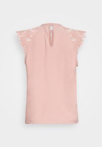 Světle růžový top bez rukávů s kulatým výstřihem. Krajkové detaily na ramenou, klíčová dírka na zadní straně a hladký povrch látky.