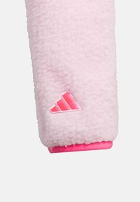 Vêtements en polaire rose avec une texture douce, dotés d'un accent rose vif à l'ourlet et d'un logo Adidas brodé en rose clair.