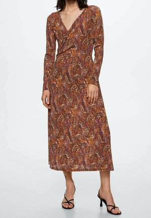 Mujer con un vestido midi de manga larga y escote en V con un patrón paisley marrón y naranja, y sandalias negras con tiras y tacón.