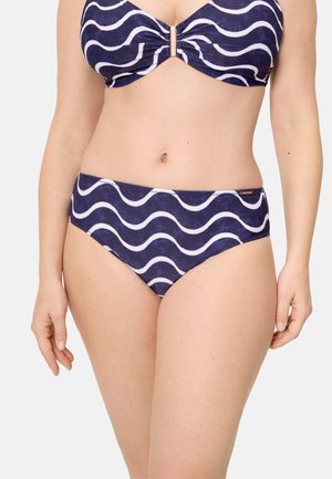 Mujer usando un bikini azul marino con rayas onduladas blancas y un broche dorado en la parte superior, mostrada desde el cuello hasta la parte superior de los muslos.