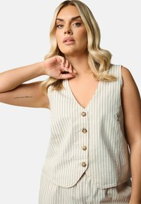 Beige ärmlös topp med vertikala marinblå ränder, V-ringning och fem knappar framtill. Tillverkad av lätt tyg med en slät textur.