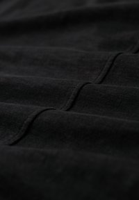 Close-up van zwarte stof met zichtbare stiksels en een gestructureerde weving, met vouwen en schaduwen op het oppervlak van het materiaal.
