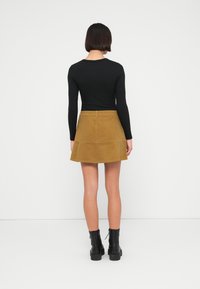 Μαύρο τοπ με μακριά μανίκια συνδυασμένο με καφέ μίνι φούστα σε καμπάνα από κορντόρι. Σημαντικές λεπτομέρειες περιλαμβάνουν φερμουάρ και υφή υφάσματος. Μαύρα μποτάκια στον αστράγαλο.