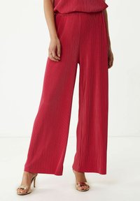 Rode wijde broek met verticale geribbelde textuur, elastische tailleband en zijzakken, gecombineerd met metallic haksandalen.