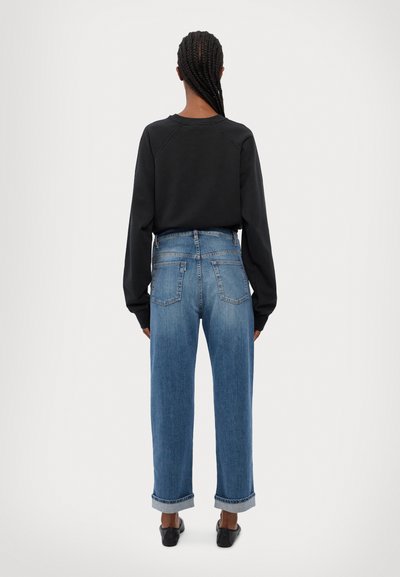 Svart hettegenser med raglanermer, kombinert med høy midje, lyseblå, vide jeans. Oppbrettede mansjetter på jeansene, minimalistisk design.