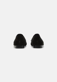 Mocassins en daim noir avec une texture lisse, un talon bas et un bout arrondi. Design minimaliste sans embellissements proéminents.