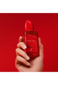 Mano sosteniendo un frasco de perfume rojo de Giorgio Armani con una tapa roja a juego sobre un fondo rojo.