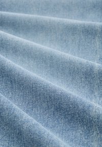 Hellblauer Denimstoff mit sichtbarer diagonaler Webstruktur, in weichen Falten gelegt.